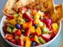 A colorful bowl of fresh fruit salsa made with strawberries, kiwi, and pineapple, served alongside golden cinnamon sugar tortilla chips on a wooden platter.