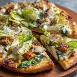 Chicken Caesar salad pizza topped with grilled chicken, romaine lettuce, parmesan cheese, and creamy dressing.
