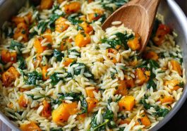 A warm bowl of creamy orzo pasta mixed with roasted butternut squash cubes and fresh spinach, garnished with Parmesan cheese and herbs.