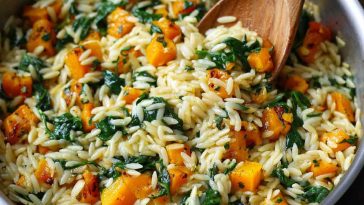 A warm bowl of creamy orzo pasta mixed with roasted butternut squash cubes and fresh spinach, garnished with Parmesan cheese and herbs.