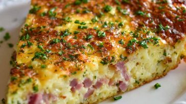 A golden-brown hash brown crust quiche filled with ham, sharp cheddar cheese, and eggs, sliced and served on a rustic plate.