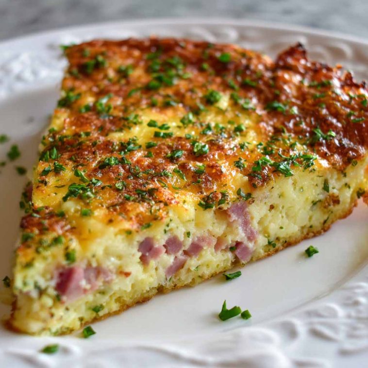 A golden-brown hash brown crust quiche filled with ham, sharp cheddar cheese, and eggs, sliced and served on a rustic plate.