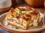 A golden-baked Monte Cristo breakfast casserole layered with ham, turkey, Swiss cheese, and custard, topped with powdered sugar and served with raspberry jam.