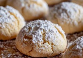 Golden pizzicati Italian pinch cookies filled with jam, lightly dusted with powdered sugar, arranged on a rustic wooden board.