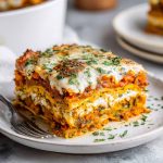 A golden-baked layered lasagna made with sweet potatoes, butternut squash, carrots, creamy sauce, and melted cheese, served in a casserole dish.