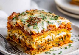 A golden-baked layered lasagna made with sweet potatoes, butternut squash, carrots, creamy sauce, and melted cheese, served in a casserole dish.