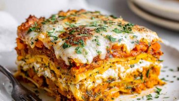 A golden-baked layered lasagna made with sweet potatoes, butternut squash, carrots, creamy sauce, and melted cheese, served in a casserole dish.