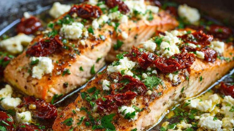 Oven-baked salmon fillets topped with crumbled feta, sun-dried tomatoes, and fresh herbs, served on a rustic platter.