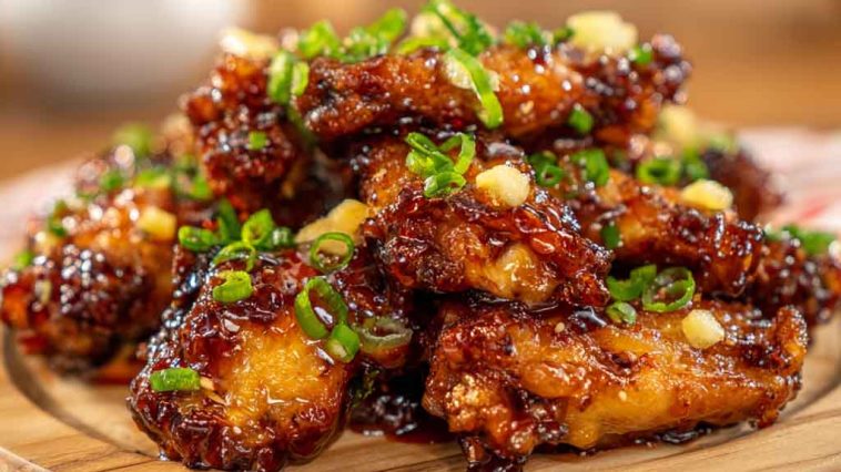 Sticky pineapple cowboy candy chicken wings glazed with sweet and spicy sauce, garnished with peppers.