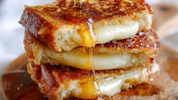 Hot honey grilled cheese sandwich with melted cheese and a drizzle of spicy honey between crispy golden bread.