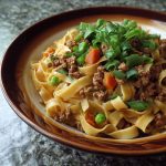 Ground pork stir-fry with flat noodles, vegetables, and a savory sauce in a wok.