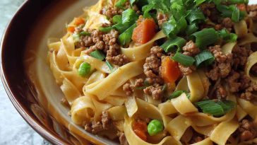 Ground pork stir-fry with flat noodles, vegetables, and a savory sauce in a wok.