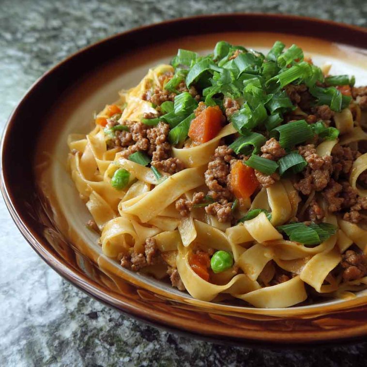 Ground pork stir-fry with flat noodles, vegetables, and a savory sauce in a wok.