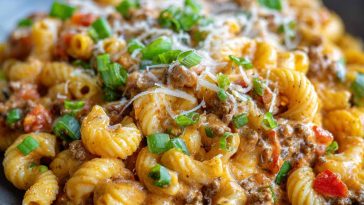 A bowl of creamy Rotel pasta with ground beef, topped with melted cheese and garnished with fresh parsley, served hot and comforting.