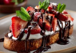 Slices of toasted baguette topped with melted chocolate, fresh strawberries, and a drizzle of chocolate sauce, arranged on a serving platter.