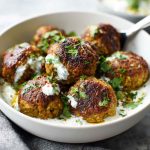 Baked Greek lentil meatballs served with creamy tzatziki sauce, fresh herbs, and a side of vegetables.