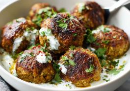 Baked Greek lentil meatballs served with creamy tzatziki sauce, fresh herbs, and a side of vegetables.