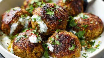 Baked Greek lentil meatballs served with creamy tzatziki sauce, fresh herbs, and a side of vegetables.