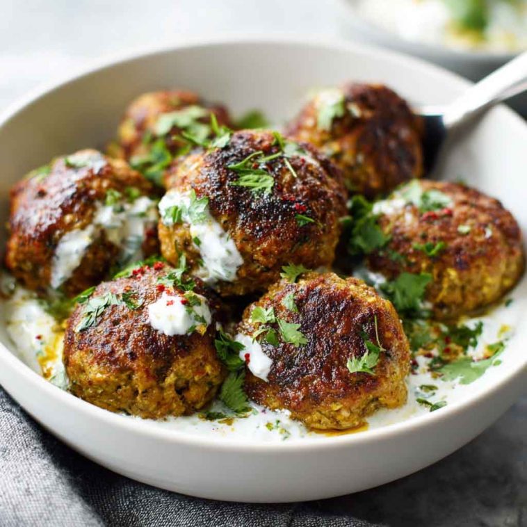 Baked Greek lentil meatballs served with creamy tzatziki sauce, fresh herbs, and a side of vegetables.