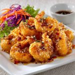 Crispy shrimp coated in a creamy honey sauce, garnished with sesame seeds and herbs.