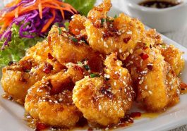 Crispy shrimp coated in a creamy honey sauce, garnished with sesame seeds and herbs.