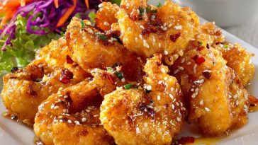 Crispy shrimp coated in a creamy honey sauce, garnished with sesame seeds and herbs.