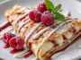 A delicate raspberry vanilla crepe folded with fresh raspberries, whipped cream, and a drizzle of vanilla sauce, served on a white plate.