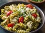 A bowl of light pesto pasta with grilled chicken strips, tossed with fresh basil pesto, cherry tomatoes, and spinach, garnished with Parmesan cheese.