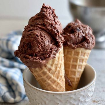 Creamy brownie batter ice cream scooped into a bowl with chocolate brownie chunks and chocolate drizzle on top.