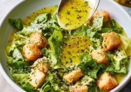 A small glass jar of homemade parmesan vinaigrette dressing with fresh salad greens in the background.