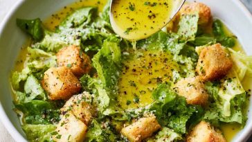 A small glass jar of homemade parmesan vinaigrette dressing with fresh salad greens in the background.