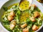 A small glass jar of homemade parmesan vinaigrette dressing with fresh salad greens in the background.