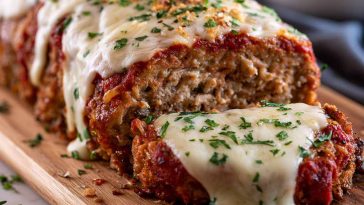 Garlic Parmesan meatloaf sliced on a plate with herbs and sauce