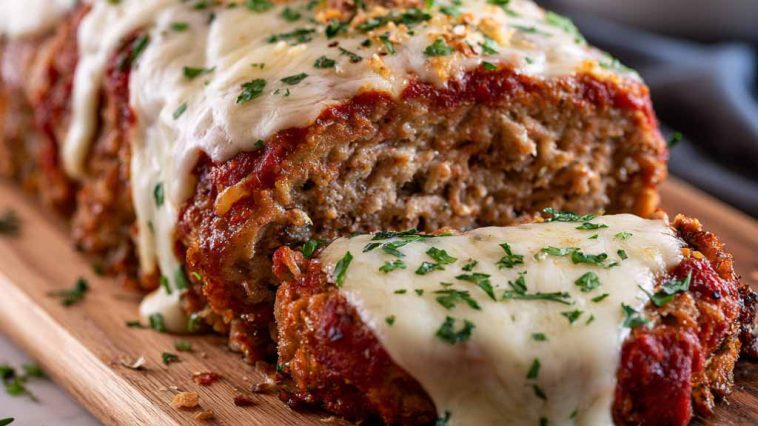 Garlic Parmesan meatloaf sliced on a plate with herbs and sauce