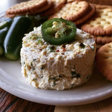 Roasted jalapeño cowboy cream cheese dip topped with crispy bacon, green onions, and melted cheese served warm with crackers.