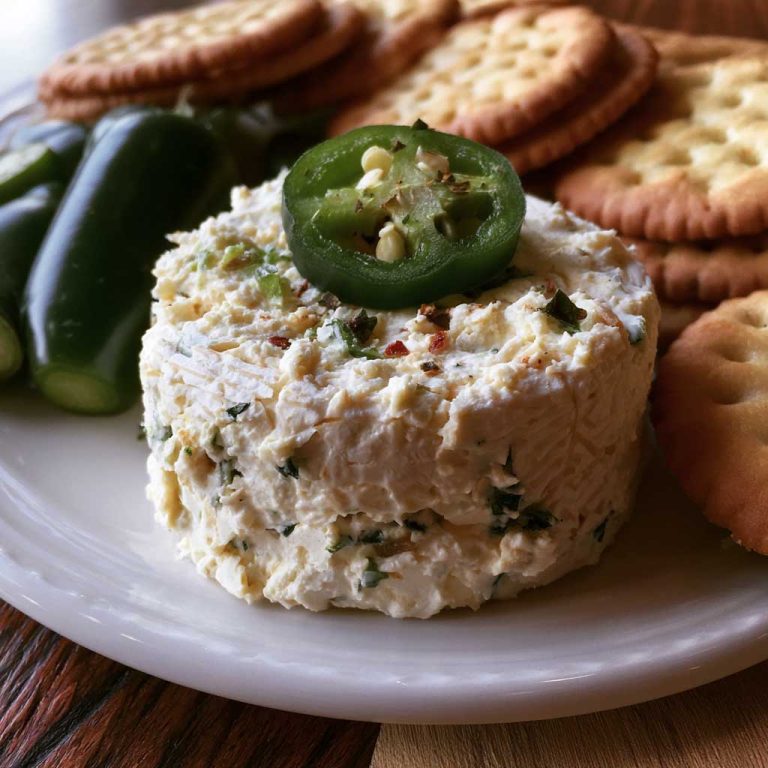 Roasted jalapeño cowboy cream cheese dip topped with crispy bacon, green onions, and melted cheese served warm with crackers.