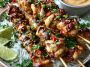 Grilled bang bang chicken skewers glazed with a creamy spicy sauce, garnished with green onions and sesame seeds.
