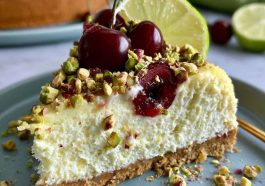 Refreshing cheesecake with layers of lemon lime filling, cherry topping, and a pistachio crust, garnished with whipped cream and chopped nuts.