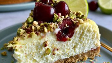 Refreshing cheesecake with layers of lemon lime filling, cherry topping, and a pistachio crust, garnished with whipped cream and chopped nuts.