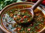 Smoky red chimichurri sauce made with roasted red peppers, garlic, herbs, and olive oil, served in a bowl with a spoon.