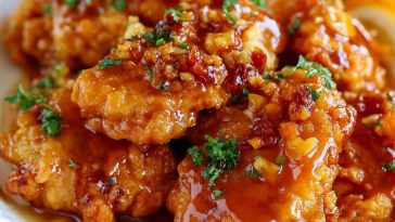 Crispy honey garlic chicken coated in a sticky sweet sauce, served hot and garnished with sesame seeds and green onions.