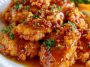 Crispy honey garlic chicken coated in a sticky sweet sauce, served hot and garnished with sesame seeds and green onions.