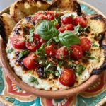 Warm caprese dip with melted mozzarella, cherry tomatoes, and fresh basil, drizzled with balsamic glaze and served with toasted bread.