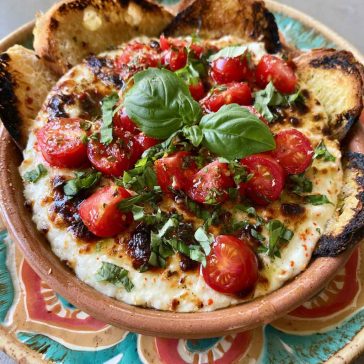 Warm caprese dip with melted mozzarella, cherry tomatoes, and fresh basil, drizzled with balsamic glaze and served with toasted bread.