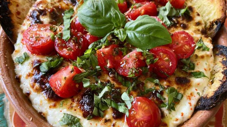 Warm caprese dip with melted mozzarella, cherry tomatoes, and fresh basil, drizzled with balsamic glaze and served with toasted bread.