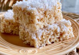 Coconut Rice Krispy treats topped with toasted coconut flakes and cut into squares on a dessert tray.