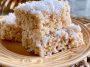 Coconut Rice Krispy treats topped with toasted coconut flakes and cut into squares on a dessert tray.