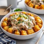 Crispy tater tots topped with sausage gravy, eggs, and melted cheese in a bowl.