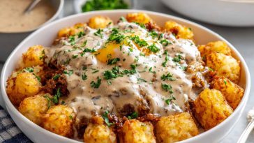Crispy tater tots topped with sausage gravy, eggs, and melted cheese in a bowl.