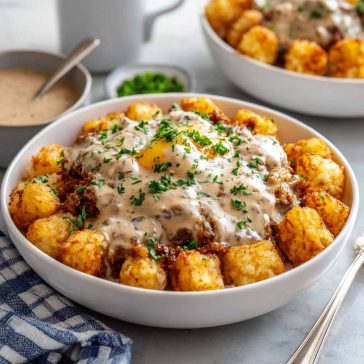 Crispy tater tots topped with sausage gravy, eggs, and melted cheese in a bowl.